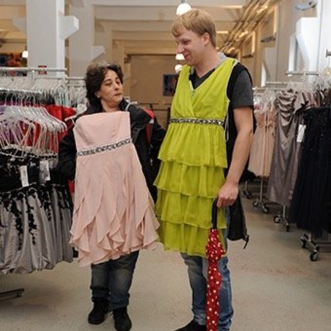Zwei Personen stehen in einem Bekleidungsgeschäft, eine trägt ein rosa Kleid, der andere ein gelbes Kleid