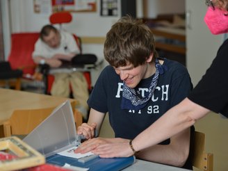 Junge arbeitet an einem Blatt Papier, gemeinsam mit einer Betreuerin
