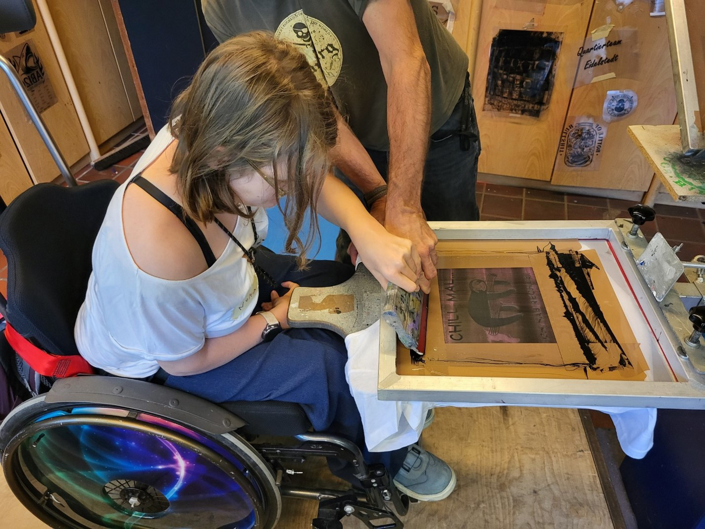 Workshop Wir machen Druck: jugendliche Teilnehmerin im Rollstuhl beim Siebdruck