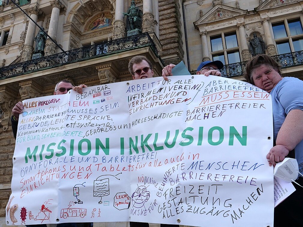 Menschen protestieren mit Plakat für Inklusion.