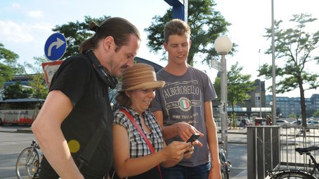 3 Menschen schauen auf ein Handy.