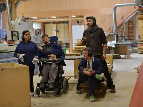 4 Personen in einer Tischlerei. Eine Person sitzt im Rollstuhl.